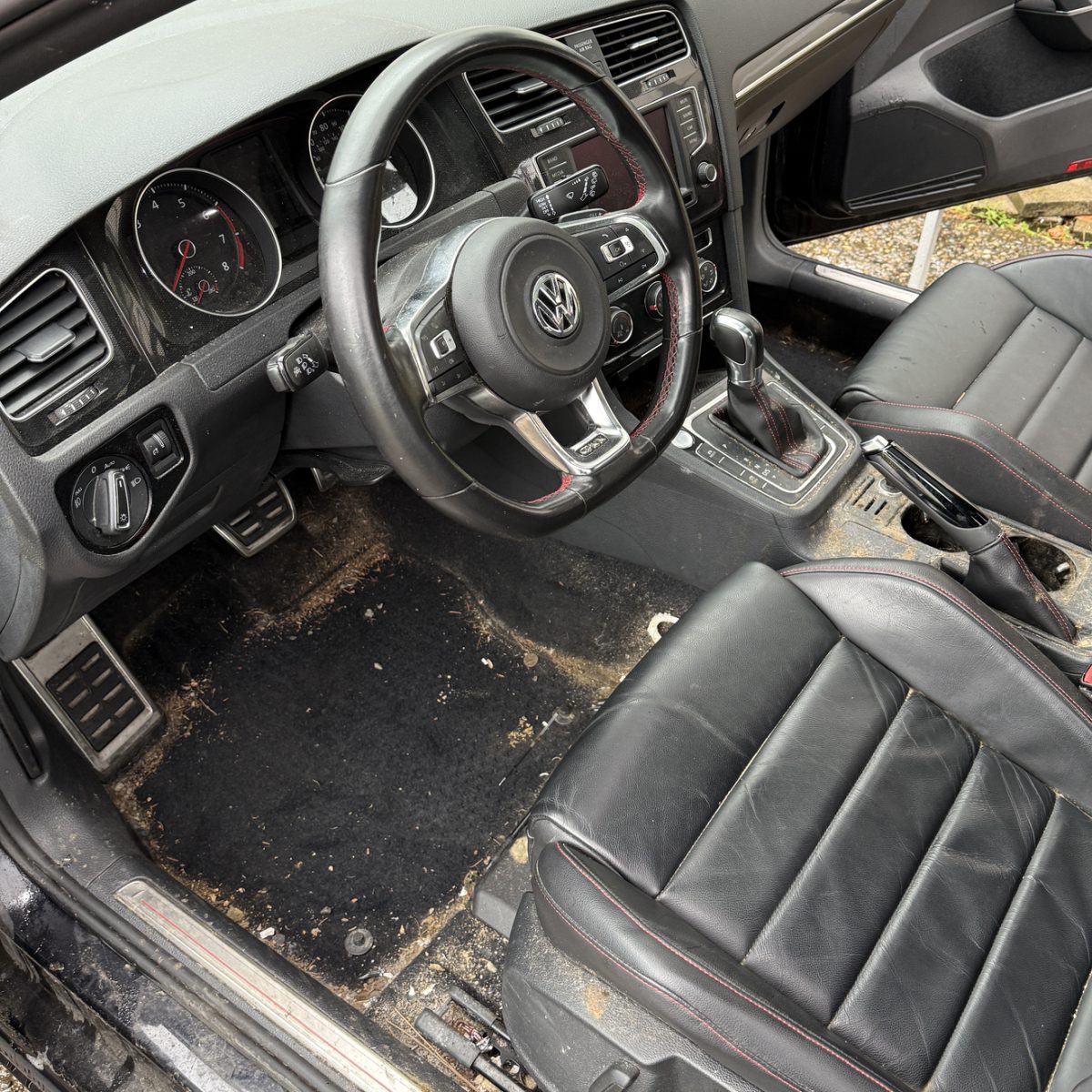 Volkswagen GTI interior before detailing, with dirt and debris covering the driver's floor